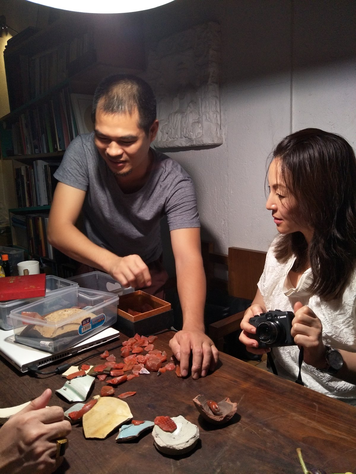 Kehan Li with a young Chinese collector examining ancient carved fragments and antique pieces laid out on a wooden table in a private collection room.
